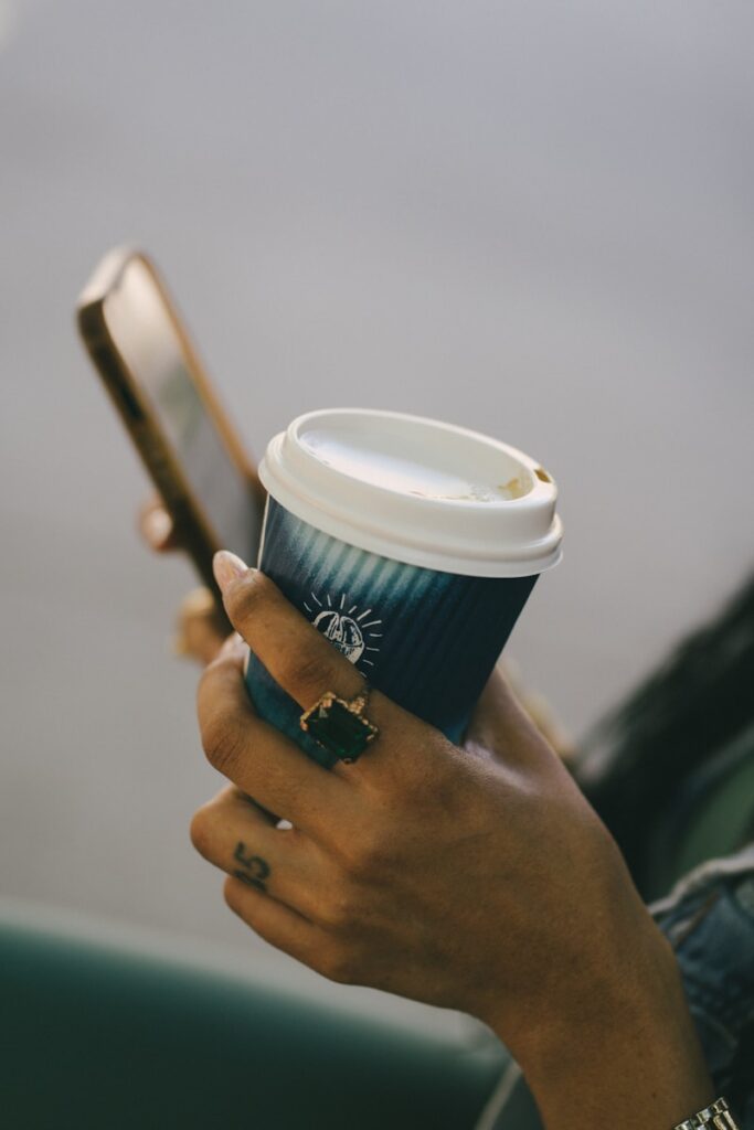 A woman holding a cup of coffee and a cell phone